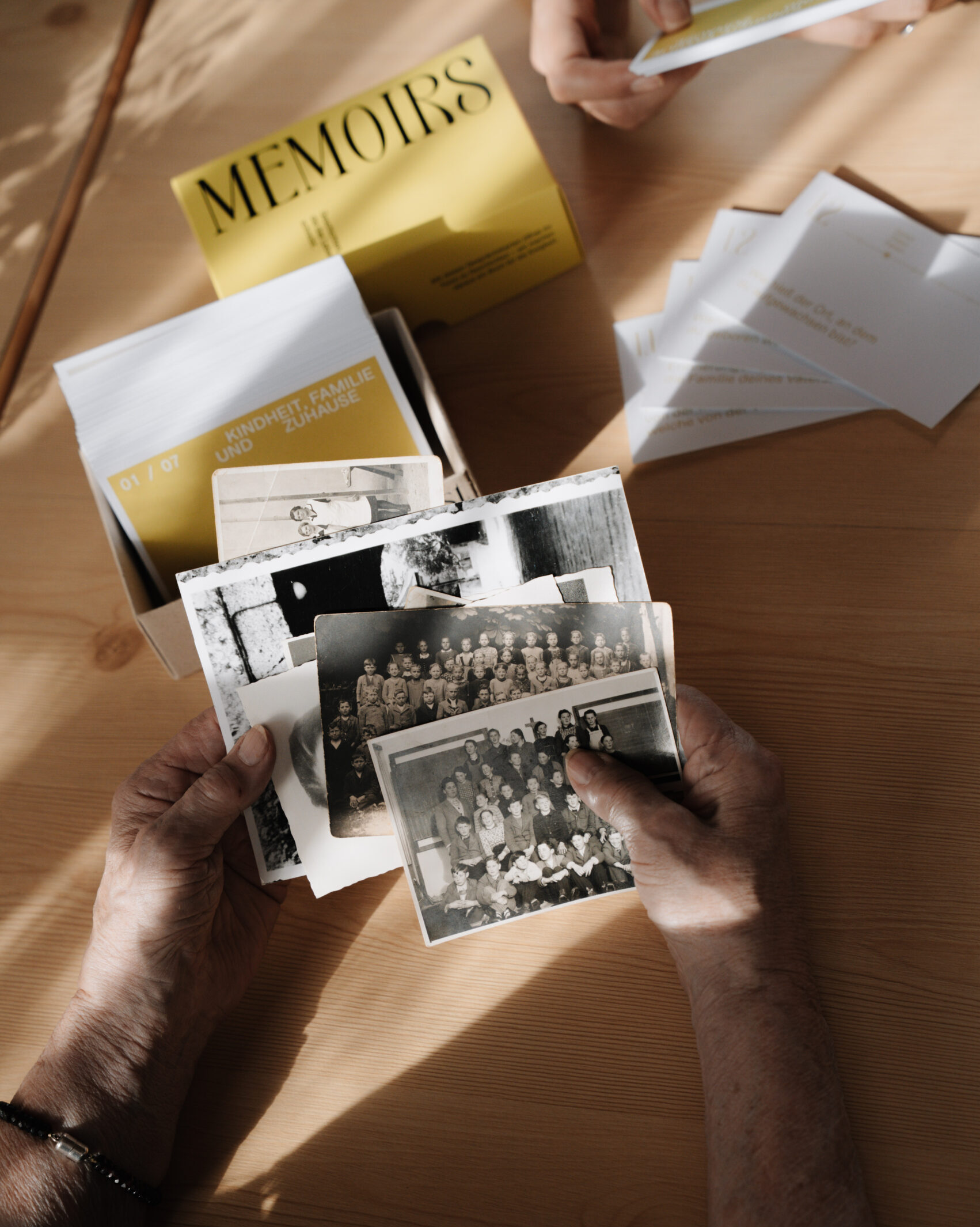 Alte Hände mit alten Fotos, im Hintergrund Memoirs Kartenset zu sehen