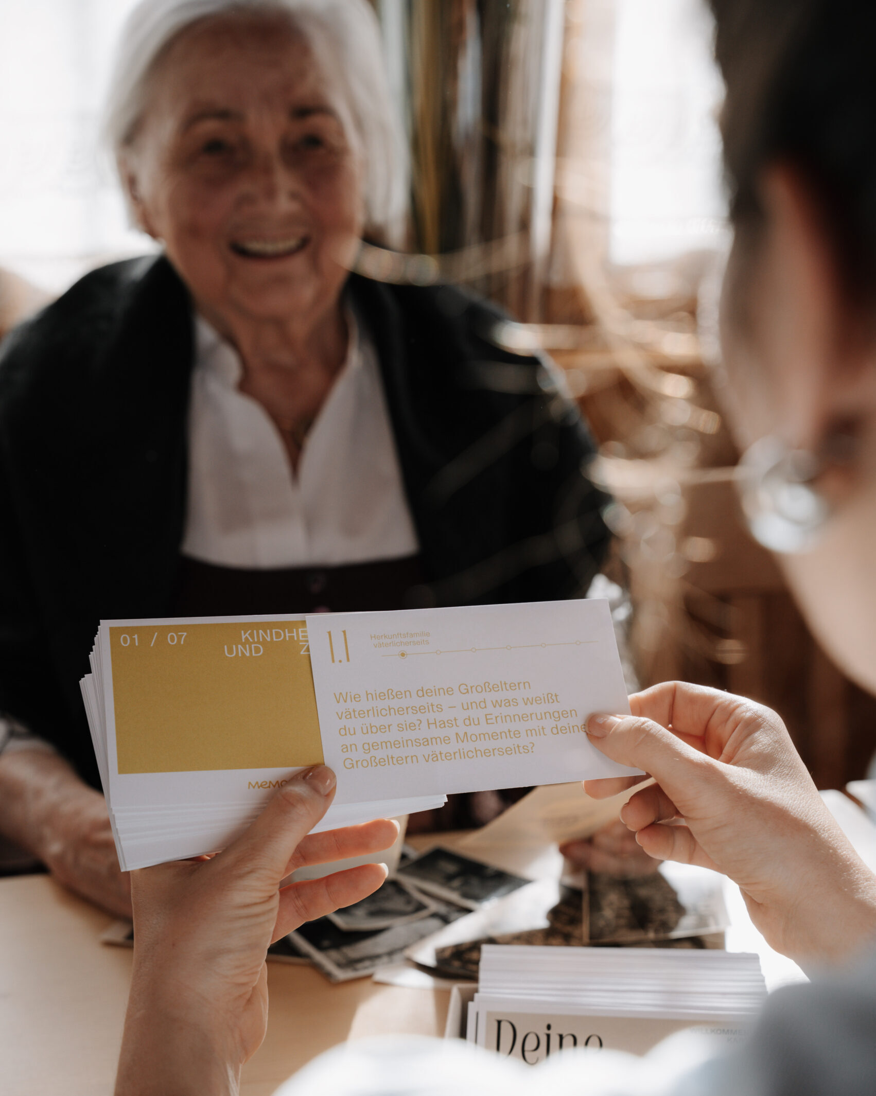Hand hält ein Memoirs-Kartenset in der Hand, im Hintergrund Oma zu sehen, jetzt erhältlich im Memoirs Shop